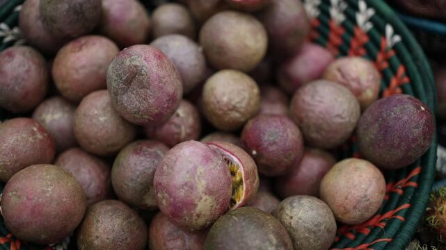 This image shows a close-up shot of passion fruits in a basket, with some fruits peeled open, revealing the inner seeds and pulp. The vibrant purple and green skin of the fruits stands out in the imag