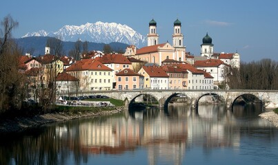 Obraz premium Scenic European town with bridge, river, church, and snowy Alps in background