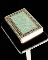 Ornate Hardcover Book on Velvet Pedestal with Intricate Cover Design Lit from Below