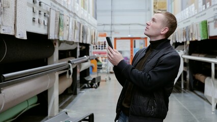 Customer browsing a smartphone app for carpet information while shopping in a home improvement store to find the perfect product. A man in a hardware store choosing flooring.
