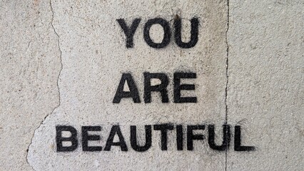 You are beautiful positive affirmation in black capital letter text sprayed on rustic, rough and...