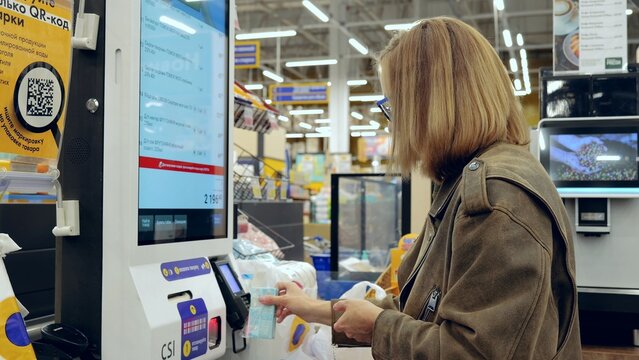 Customer making a contactless payment with smartphone at self service checkout in modern grocery store - Powered by Adobe