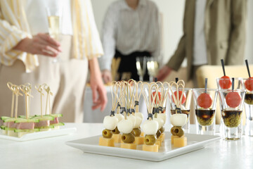 Many different tasty canapes on white table. People enjoying buffet meals indoors, closeup