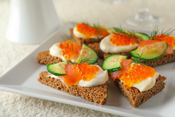 Tasty canapes with salmon and cucumber on white table, closeup