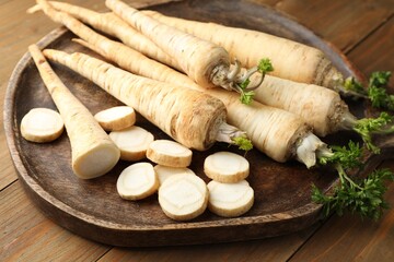 Whole and cut fresh parsley roots on wooden table, closeup