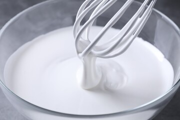 Mixing whipped cream in bowl with whisk on grey table, closeup