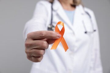 Multiple Sclerosis awareness. Doctor with orange ribbon on light grey background, closeup