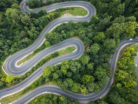 zenithal aerial view of a winding 180-degree curved road in a green forest while cars pass by on the road in Romania.