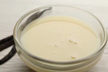 Tasty condensed milk and vanilla pods on white wooden table, closeup