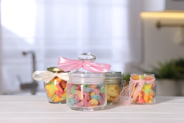 Tasty gummy candies in jars on light wooden table indoors