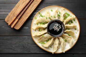 Tasty boiled gyoza (dumplings) with green onion served on black wooden table, flat lay