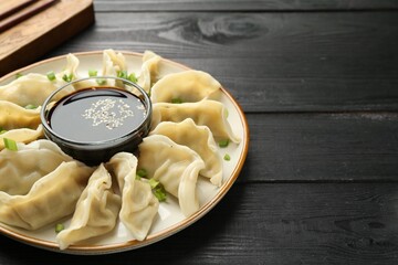 Tasty boiled gyoza (dumplings) with green onion served on black wooden table, closeup. Space for text