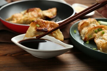Dipping tasty fried gyoza (dumpling) into soy sauce on wooden table, closeup
