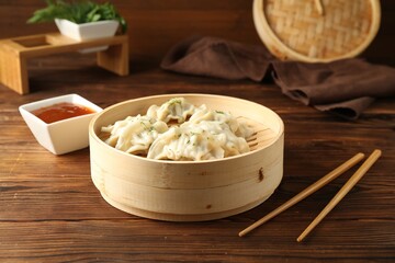 Tasty boiled gyoza (dumplings) in bamboo steamer, sauce and chopsticks on wooden table