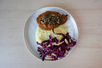 A plate of pork schnitzel with mash potato and red cabbage slaw.