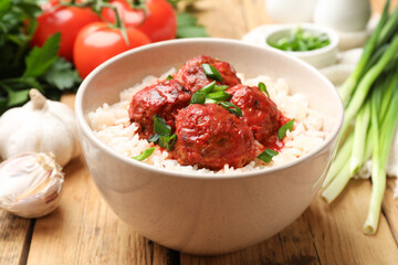 Tasty meatballs with sauce, rice and products on wooden table, closeup