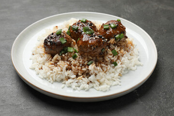 Delicious rice with meatballs, sauce and green onions on black table, closeup