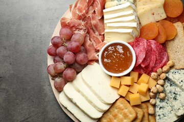 Different types of cut cheese and other snacks on grey textured table, top view. Space for text