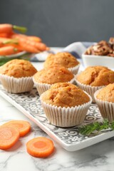 Tasty carrot muffins, fresh vegetables and walnuts on white marble table, closeup