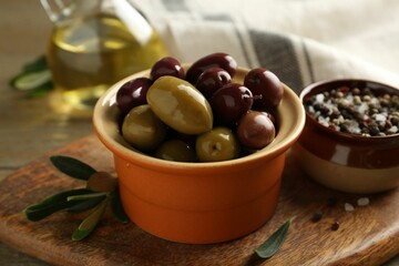 Tasty olives in bowl, leaves and spices on wooden table, closeup