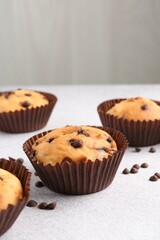 Delicious muffin with chocolate chips on light grey table, closeup