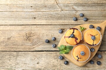 Delicious muffins with blueberries and mint on wooden table, flat lay. Space for text