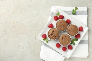 Delicious muffins with raspberries and mint on grey textured table, top view. Space for text