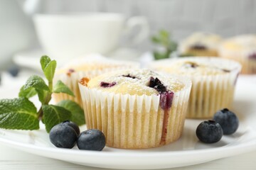 Delicious muffins with blueberries, powdered sugar and mint on white table, closeup