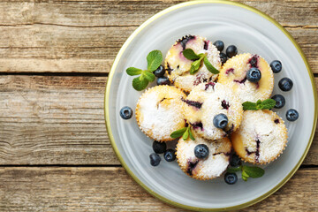 Delicious muffins with blueberries, powdered sugar and mint on wooden table, top view. Space for text