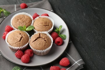 Delicious muffins with raspberries and mint on dark textured table, closeup. Space for text