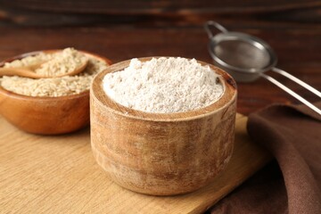 Brown rice, flour and sieve on wooden table, closeup