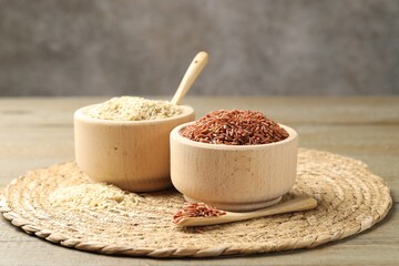 Different sorts of raw brown rice on wooden table against grey background, closeup.