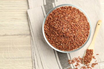 Brown rice in glass bowl and spoon on wooden table, flat lay. Space for text