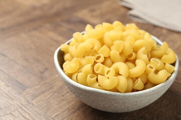 Raw horns pasta in bowl on wooden table, closeup