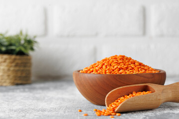 Wooden bowl brimming with rustic red lentils, wooden scoop nestled alongside, spilling grains