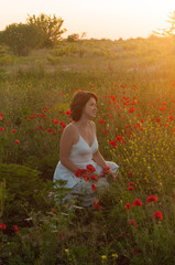 Beautiful blonde girl in a white dress on the poppy field at sunset