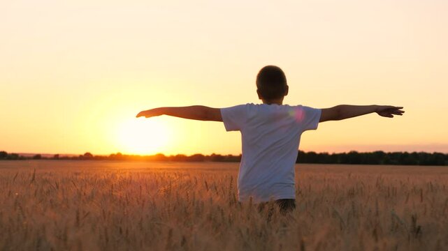 Happy male teen running on wheat field with open hands enjoy freedom at sunset sunrise back view closeup. Boy kid teenager relaxing imagine flying at dusk rye meadow sun sky forest horizon