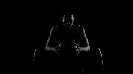 Basketball player sitting on a bench. Concentrated african american sports man against black background.