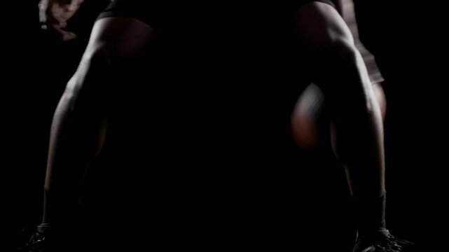 Basketball player bouncing a ball. African american sports man practicing against black background. Abstract body shot front view.