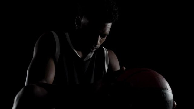 Basketball player sitting on a bench taking deep breath in. Concentrated african american sports man against black background.
