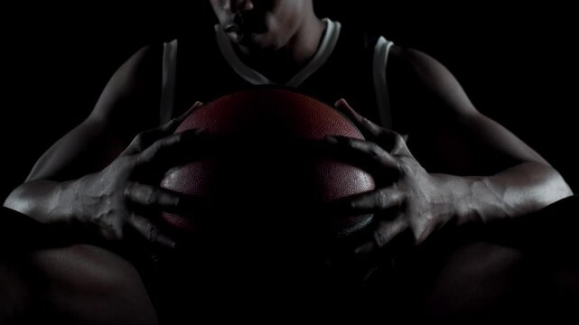 Basketball player sitting on a bench looking down. Concentrated african american sports man against black background.