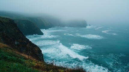 A rugged coastline covered in thick fog, with waves crashing against the cliffs