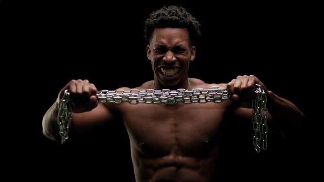 Muscular man showing muscles and holding a chain. African American male posing against black background.
