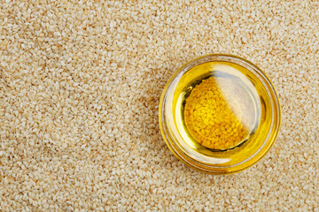 Glass bowl containing golden sesame oil placed on seeds top view