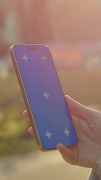Vertical Screen: Green screen smartphone display featuring female user standing outdoors with mobile device against blurred natural background during golden light