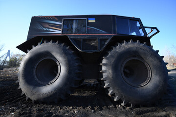 An unusual amphibious vehicle features huge tires, designed for rugged terrain. It stands out against a blue sky in an outdoor area, showcasing its distinctive look © Oleksandr Zinchenko