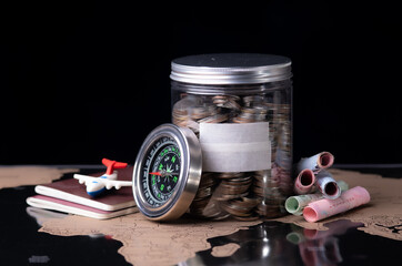 Holidays money savings in a glass jar with compass, passport travel document on world map, close-up. Travel budget concept.