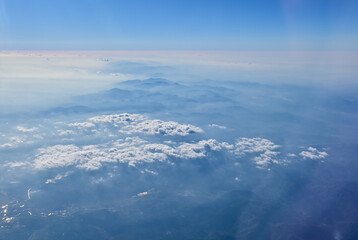 The view of the stunning landscape with mountains and clouds from the airplane window. Aerial view of the natural scene, mountain range. Travel and landscape scene. Travel and nature concept. 