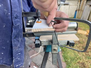 Close up of a caucasian man's hands using a coping saw to cut the curved edge of a length of wooden...