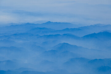 The view of the stunning landscape with mountains and clouds from the airplane window. Aerial view of the natural scene, mountain range. Travel and landscape scene. Travel and nature concept. 